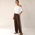 Modelo de frente con pantalón plisado chocolate, franja lateral visible de cadera a tobillo con orilla de encaje