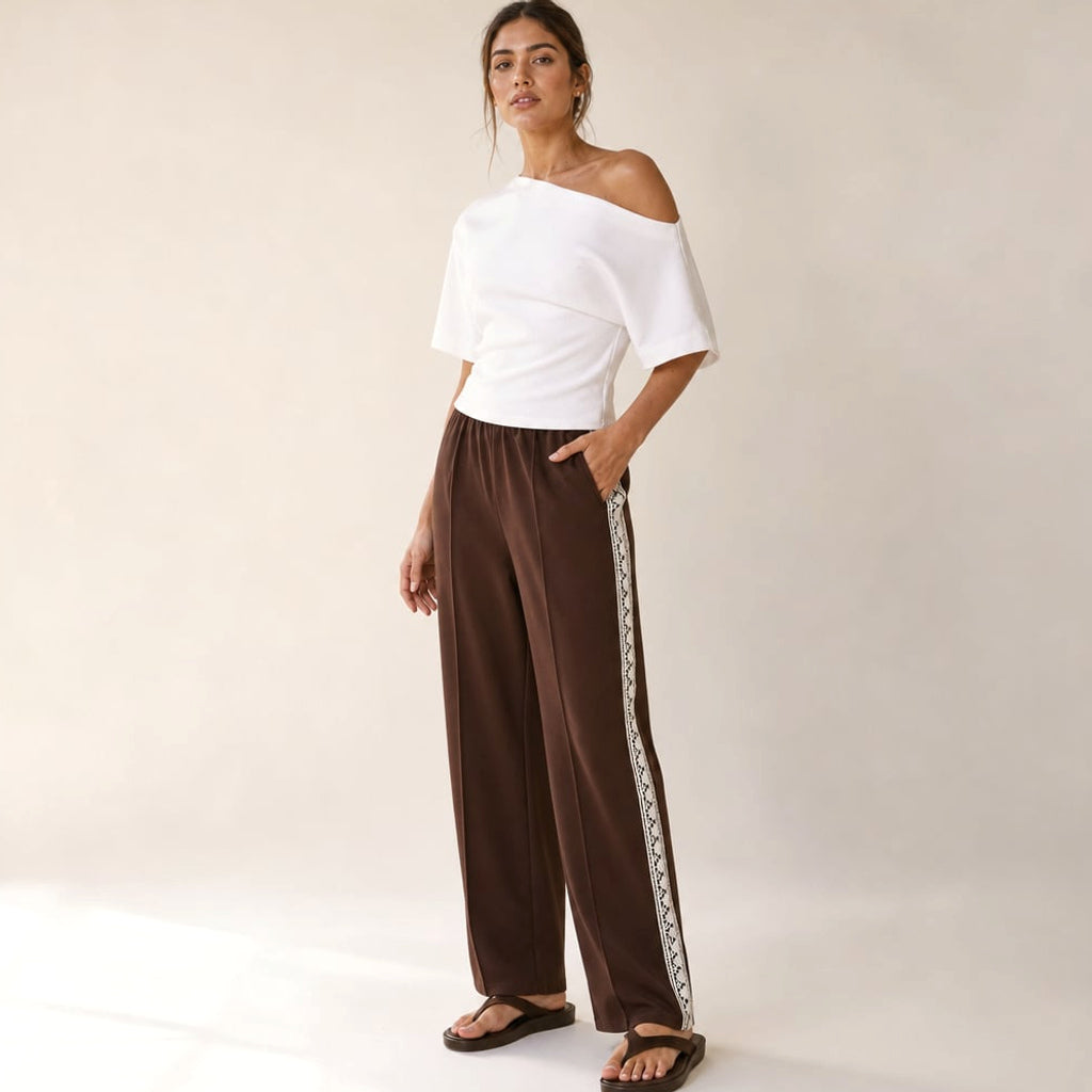Modelo de frente con pantalón plisado chocolate, franja lateral visible de cadera a tobillo con orilla de encaje