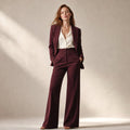 Modelo vistiendo conjunto sastre borgoña de blazer entallado con solapas picudas y pantalón de pierna ancha de tiro alto, silueta completa