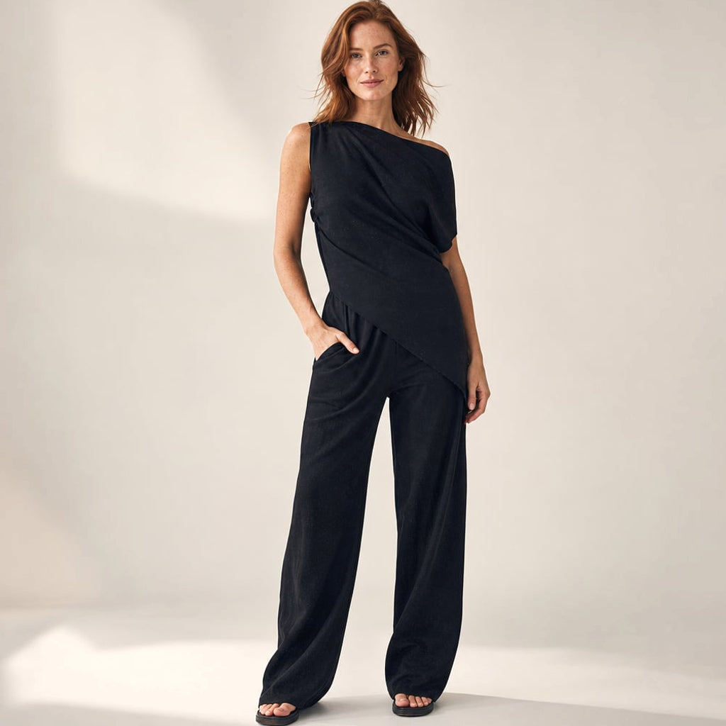 Modelo viste co-ord negro de hombro asimétrico y pantalón wide-leg hasta el piso